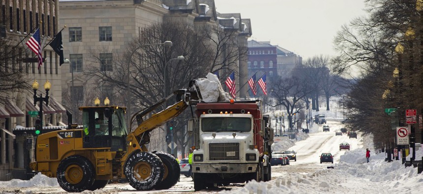 Heavy equipment fills a dump truck with snow as clearing begins Monday on 15th Street near the White House in Washington, D.C. Post-blizzard, residents face slippery roads, spotty transit service, mounds of snow, and closed schools and government offices.