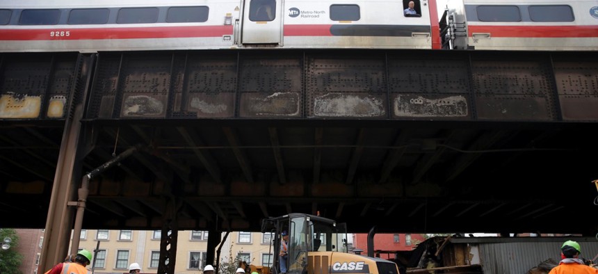 While a Metro-North train passes above, work continues underneath the tracks at the site of a fire in New York on Wednesday.