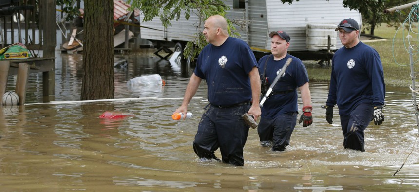 Bridgeport, W.Va., firefighters, Steve Gallo, left, and Ryan Moran, center, are joined by an unidentified co-worker as they walk through a flooded street while searching homes in Rainelle, W. Va., Saturday, June 25, 2016.