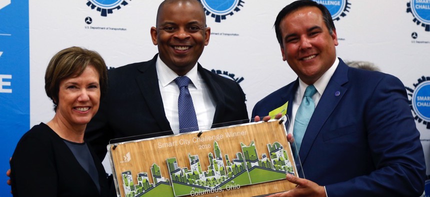Barb Bennett, left, president/COO of Vulcan Inc., and U.S. Transportation Secretary Anthony Foxx, center, present the Smart City Challenge award to Columbus, Ohio Mayor Andrew Ginther.