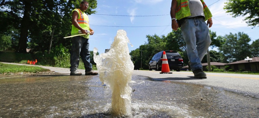 Des Moines Water Works employees walk past water bubbling through a hole in a street following a water main break in 2015. After decades of deferring maintenance, scores of World War II-era drinking water systems are in need of replacement.
