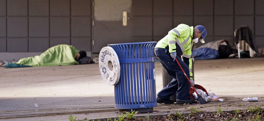 A contract worker cleans-up trash as men sleep behind him under an overpass near The Jungle encampment in Seattle. 