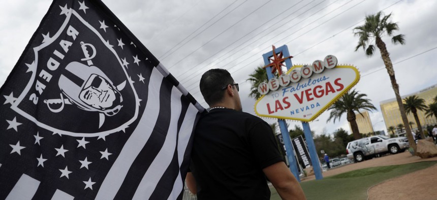 Matt Gutierrez carries a raiders flag by a sign welcoming visitors to Las Vegas.