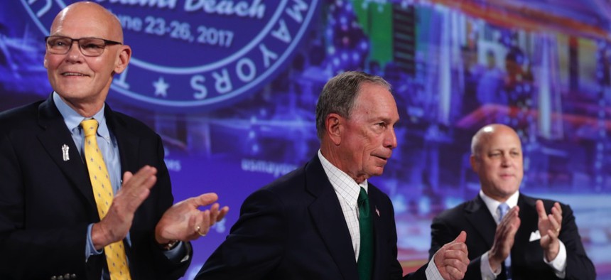 Michael Bloomberg, center, gestures as James Carville, left, and New Orleans Mayor Mitch Landrieu, right, applaud after his speech at the annual U.S. Conference of Mayors meeting Monday in Miami Beach, Fla.