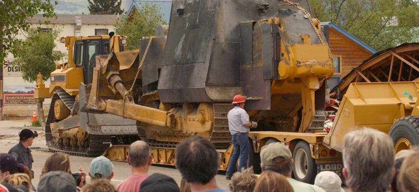 A crowd of onlookers watches as a makeshift armored bulldozer is loaded onto a tractor-trailer after being extracated from the rubble of a warehouse in Granby, Colo., Saturday afternoon, June 5, 2004.