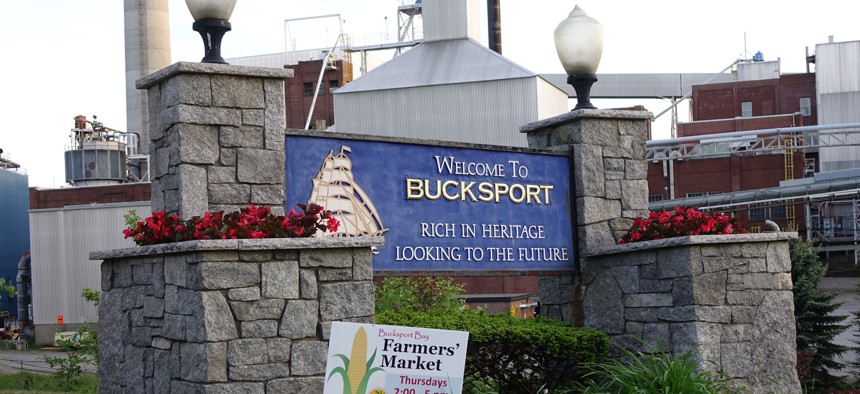 A welcome sign in Bucksport, Maine stands in front of the former Verso paper mill, now demolished. 