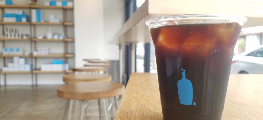 A cup of cold brew coffee and interior view of a Blue Bottle Coffee Co. location in Los Angeles.