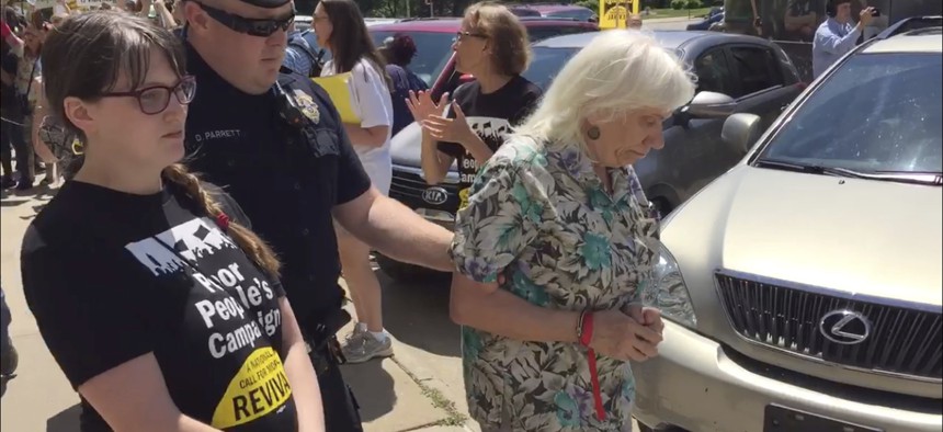 A Capitol Police officer escorts two protesters out of the Kansas secretary of state's office and toward a bus waiting to take them to the local jail, Monday, May 21, 2018, in Topeka, Kan.