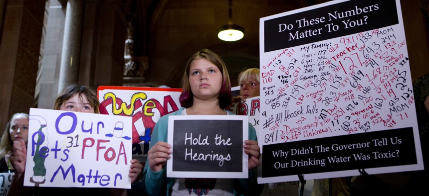 n this June 15, 2016 file photo, Hoosick Falls residents hold signs during a news conference at the state Capitol in Albany, N.Y., calling for hearings on the state's handling of PFOA contamination in drinking water in their town. New York environmental r