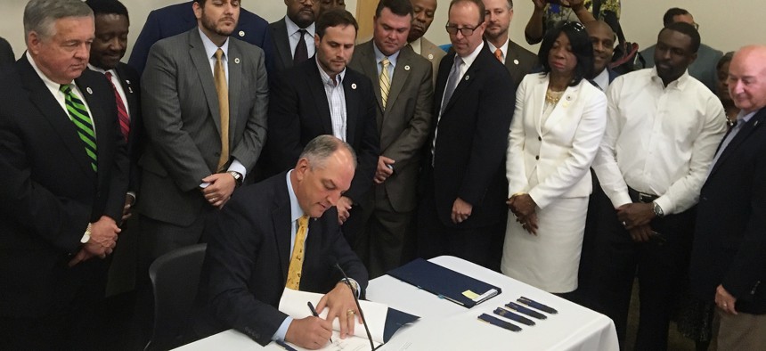 In this June 15, 2017 photo, a bipartisan group of lawmakers surround Louisiana Gov. John Bel Edwards as he signs 10 criminal justice bills into law during a ceremony in Baton Rouge, La. 