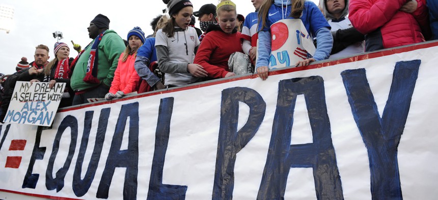 In this April 6, 2016, file photo, fans stand behind a large sign for equal pay for the women's soccer team during an international friendly soccer match between the United States and Colombia at Pratt & Whitney Stadium in East Hartford, Conn.