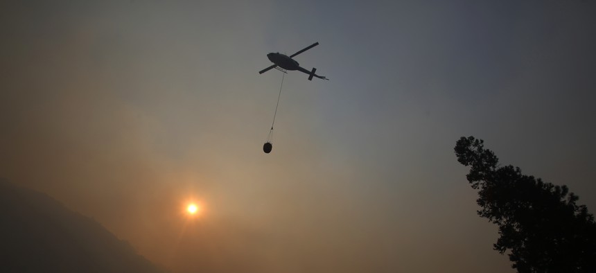 A fire helicopter takes off through smoke rising to make a drop on active fires in Yosemite National Park after the park reopened after a three week closure from smoke and fires on Tuesday, Aug. 14, 2018.