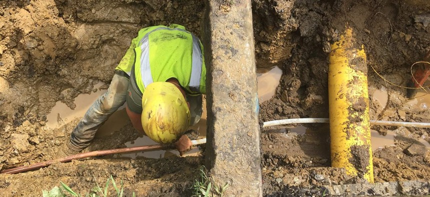After digging out the road and lawn, a worker ducks under the curb while connecting a copper pipe on private property with a Pex tube on public property.