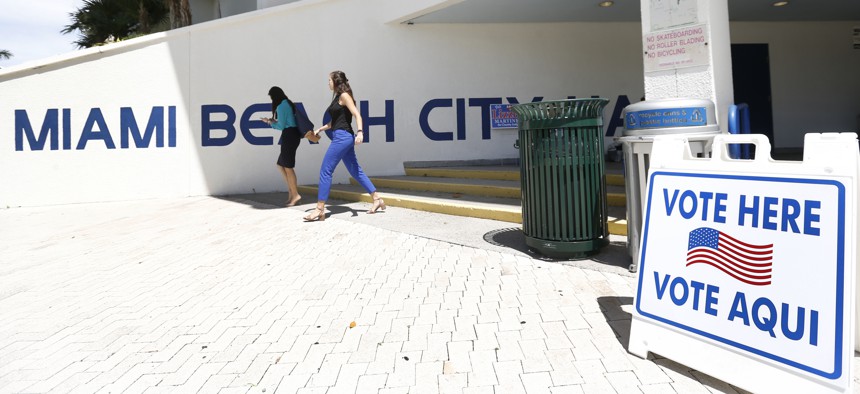 Pedestrians walk past a sign for a polling station at Miami Beach City Hall, Monday, Aug. 13, 2018, in Miami Beach, Fla.