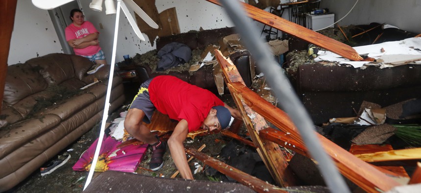 Dorian Carter looks under furniture for a missing cat after several trees fell on their home during Hurricane Michael in Panama City, Fla., Wednesday, Oct. 10, 2018.