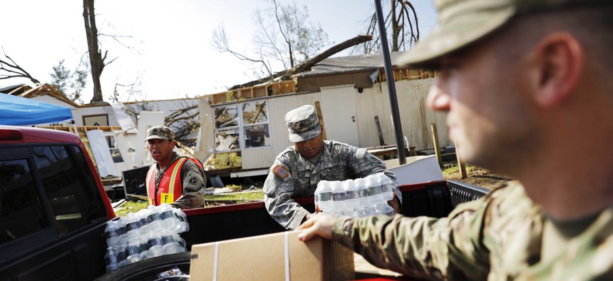 A damaged home stands in the background as soldiers with Florida National Guard's Bravo Company, 2nd Battalion, 124th Infantry Regiment, load food and water for the public at an aid distribution point in the wake of Hurricane Michael in Panama City, Fla.
