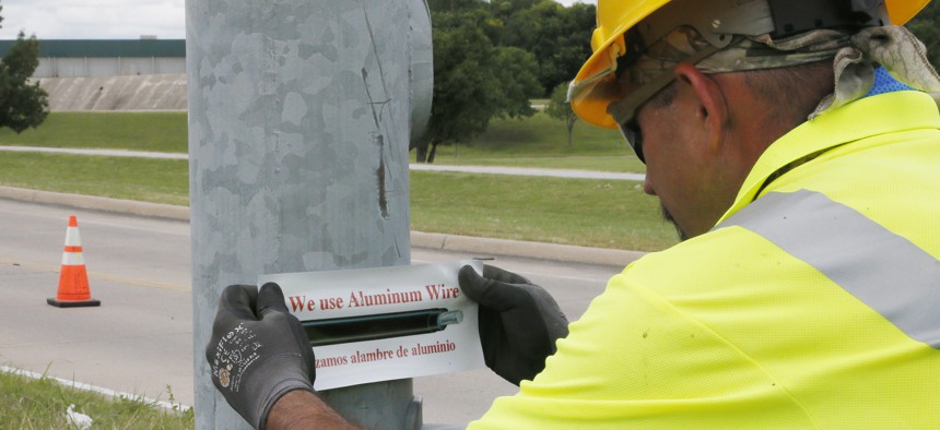 In this Thursday, June 22, 2017 photo, David Tubb puts a sticker on the base of a streetlight where new aluminum wiring has been installed in Tulsa, Okla. The city has lost 33 miles of streetlight wiring to thieves stealing copper wire.