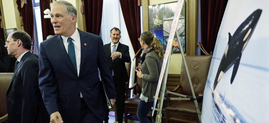 Washington Gov. Jay Inslee walks past a photo of an orca whale after he talked to reporters about his 2019-2021 budget proposal, Thursday, Dec. 13, 2018, at the Capitol in Olympia, Wash.