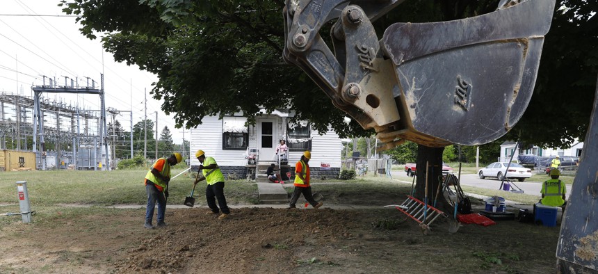 In this July 20, 2018, file photo, workers back fill a hole used to replace lead pipe with copper water supply lines to a home in Flint, Mich. 