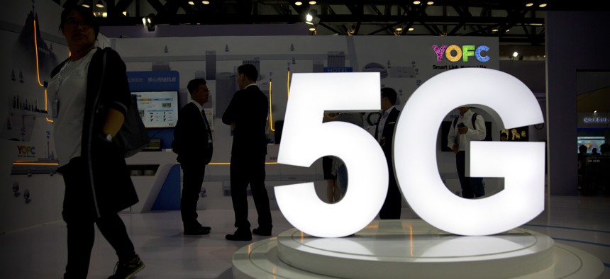 Visitors stand near a 5G logo at a display for Chinese fiber optic cable maker YOFC at the PT Expo in Beijing, Sept. 26, 2018. 