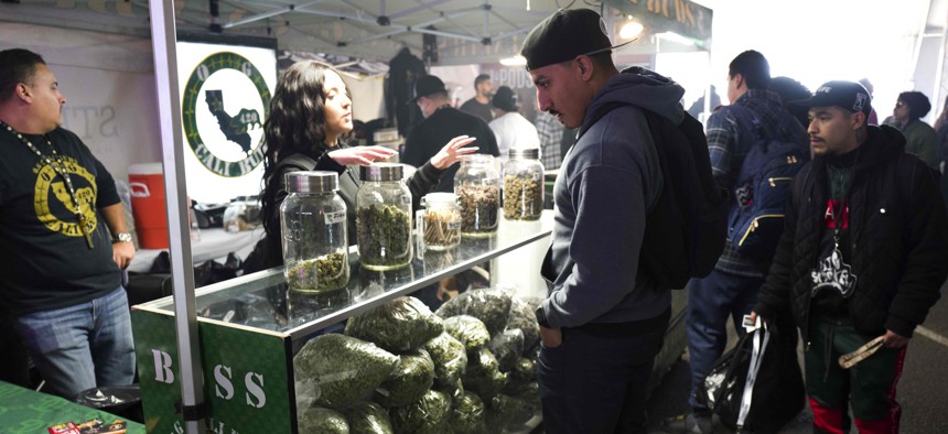 In this Saturday, Dec. 29, 2018 photo a bud tender offers cannabis by Boss Status Genetics from a display filled with large bags of marijuana during Kushstock 6.5 festival in Adelanto Calif. 