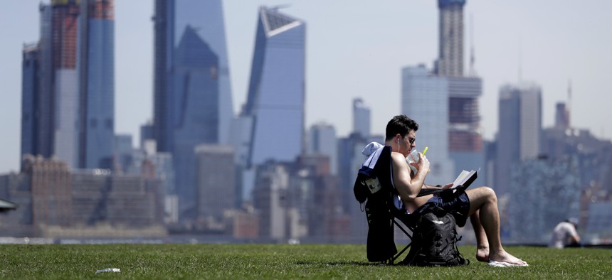 Part of the New York City skyline gives backdrop to a man as he sips on a drink while sunbathing on a warm day at Pier A Park on May 2, 2018, in Hoboken, N.J.