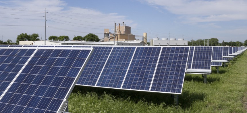 In this May 31, 2018, photo, a solar panel array collects sun light with the Fremont, Neb., power plant seen behind it.