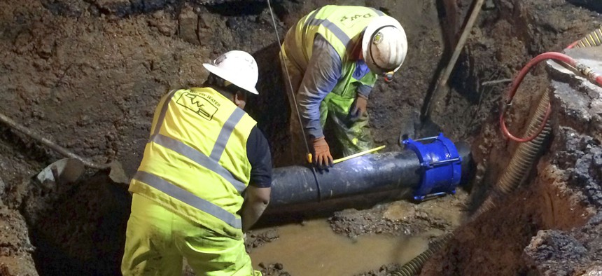 Los Angeles Department of Water and Power (DWP) workers install a segment of replacement pipe as they repair a water main rupture that created a large sinkhole on Wildomar Street in the Pacific Palisades area of Los Angeles on May 25, 2018.