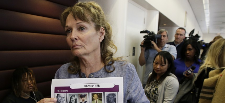 In this May 14, 2018, file photo, Melanie Barbeau displays photos of murder victims believed to be slain by the Golden State Killer as she leaves a hearing for suspect Joseph DeAngelo in Sacramento, Calif.