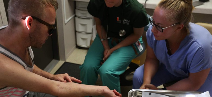 Two University of Miami medical students examine the track marks of a patient at the IDEA Exchange, which offers free wound care and HIV screenings. Southern states are beginning to embrace harm reduction techniques, including needle exchanges.