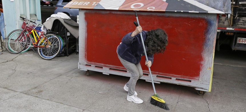 A woman sweeps outside her plywood home along Division Street Friday, Feb. 26, 2016, in San Francisco.