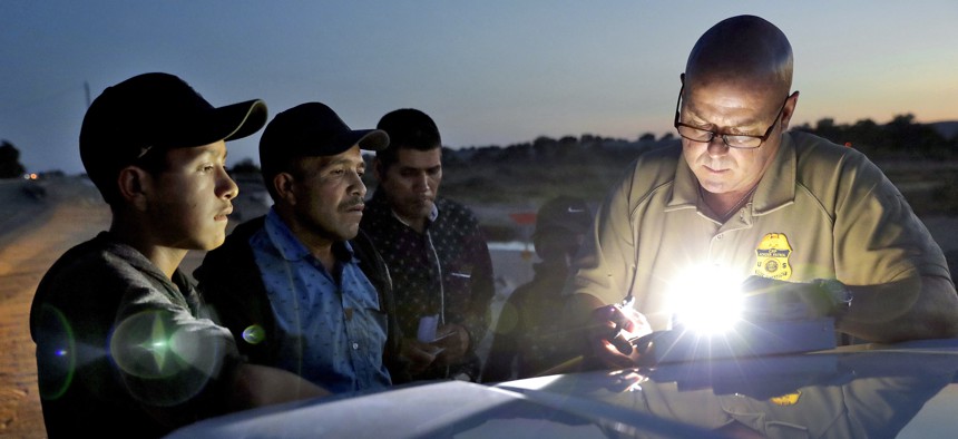In this July 18, 2018, file photo, a U.S. Customs and Border Patrol agent gathers information on four Guatemalan nationals, including two men and a pair of 12 and 13-year-old boys in Yuma, Ariz. 