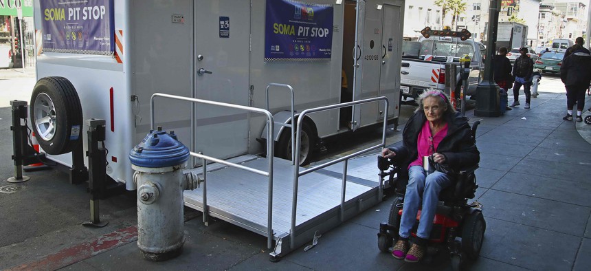 In this photo taken on Thursday, April 26, 2018, a woman in a wheelchair passes a "Pit Stop" public restroom facility in San Francisco.