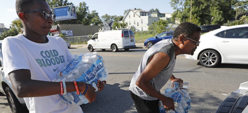 Volunteer Matthew Tiggs, left, helps Newark resident Mack Mayton load cases of bottled water into the trunk of his car, Aug. 12, 2019, in Newark, N.J., after Mayotn picked it up at the Boylan Street Recreation Center. 
