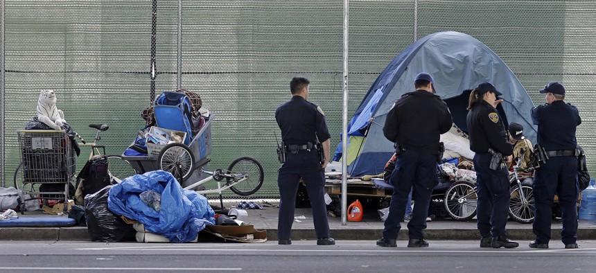 San Francisco police officers wait while homeless people collect their belongings.  In June, city officials adopted legislation to set up a program allowing people with mental illness and addiction to be forced into treatment.  