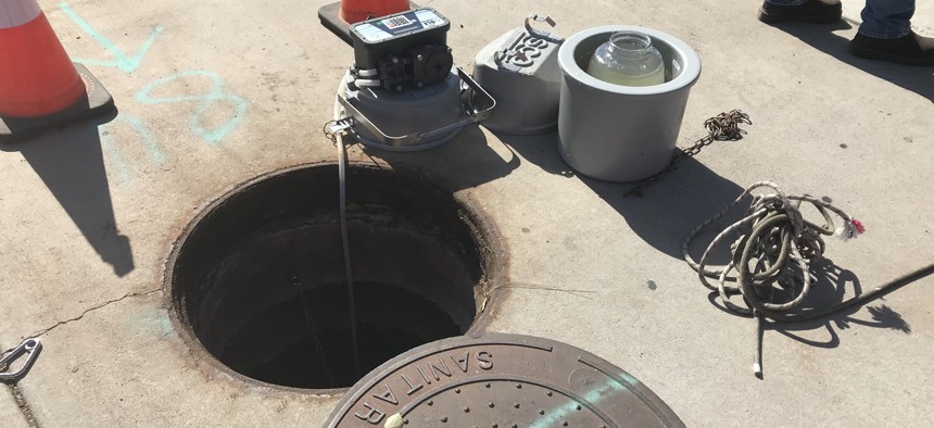 A sampler tapping directly into the sewer through a manhole in Tempe, Arizona. A glass jar of wastewater is also pictured.