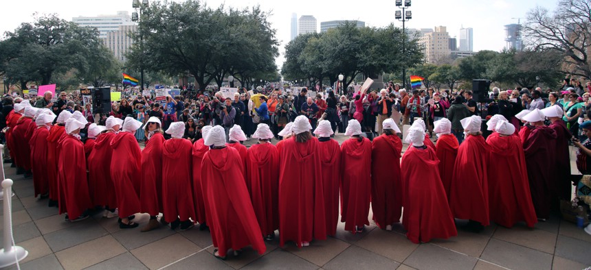 Women dressed in "Handmaids Tale" costumes stand on the steps of the state Capitol at the start of a rally for reproductive rights.