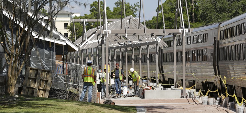 In this Monday, Oct. 28, 2013 photo, construction workers make progress on the SunRail station as an Amtrak train stops at the next door Amtrak station to pick up passengers in Winter Park, Fla. 