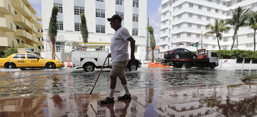 A man walks along a flooded street in Miami Beach, Fla.