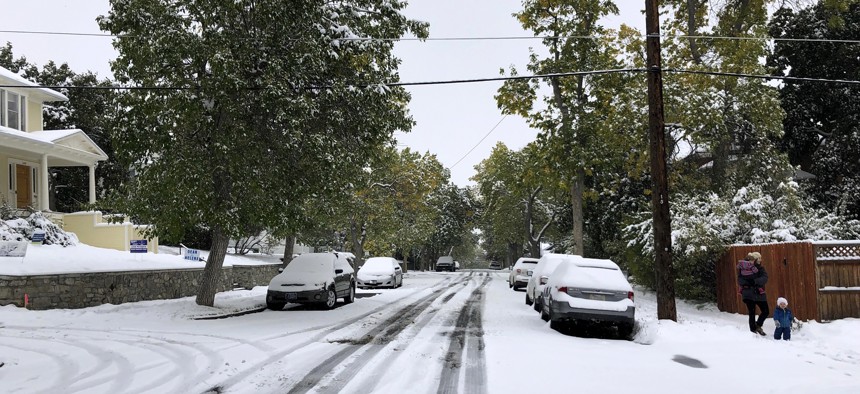 Pedestrians make their way along a snow covered street lined with trees that still have their leaves during a fall snowstorm in Helena, Mont., on Sunday, Sept. 29, 2019. 
