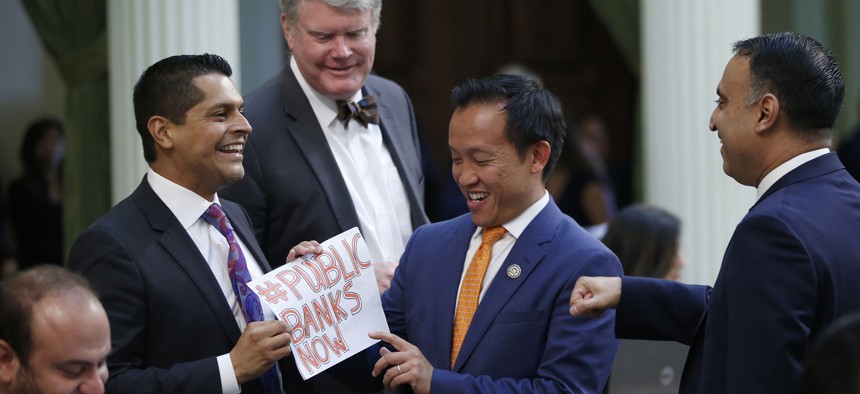 Assemblyman Miguel Santiago left, presents Assemblyman David Chiu, third from left, a note reading #PUBLIC BANKS NOW after Chiu's measure to let California cities create public banks, was approved by the Assembly on Sept. 13, 2019.