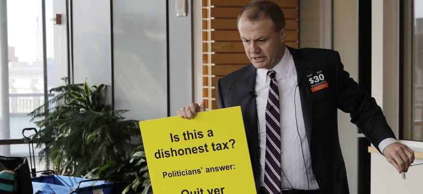 Anti-tax activist Tim Eyman holds a sign as he prepares to talk to reporters, Thursday, Nov. 7, 2019, outside the office of Seattle Mayor Jenny Durkan in Seattle. 