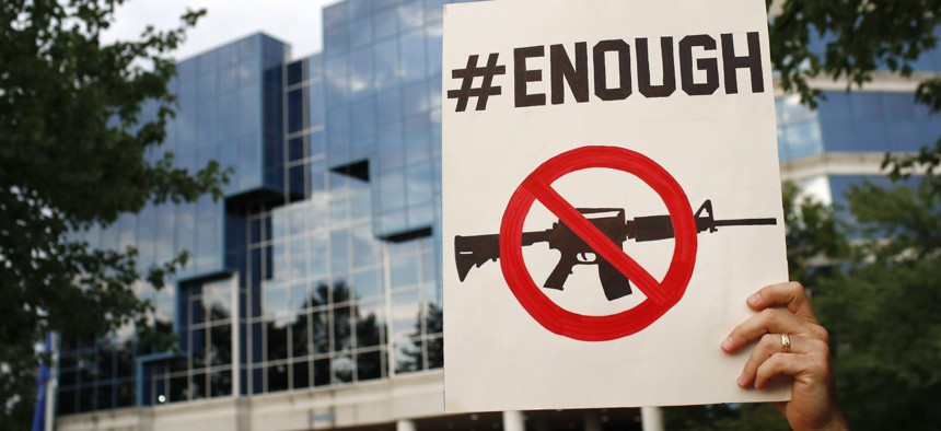 Protester Matt McCabe holds a sign outside the National Rifle Association's headquarters building during a vigil for recent victims of gun violence, Monday, Aug. 5, 2019, in Fairfax, Va.