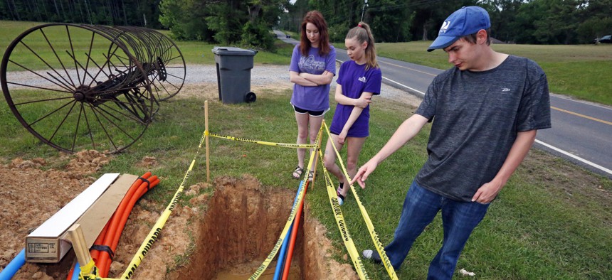 In this May 8, 2019, photograph, Riley Shaw, right, and his youngest sister, Leah, center, and his twin, Abigail, stand around a fiber-optic line that is expected to bring the Shaw family internet service to their home outside Starkville, Miss.