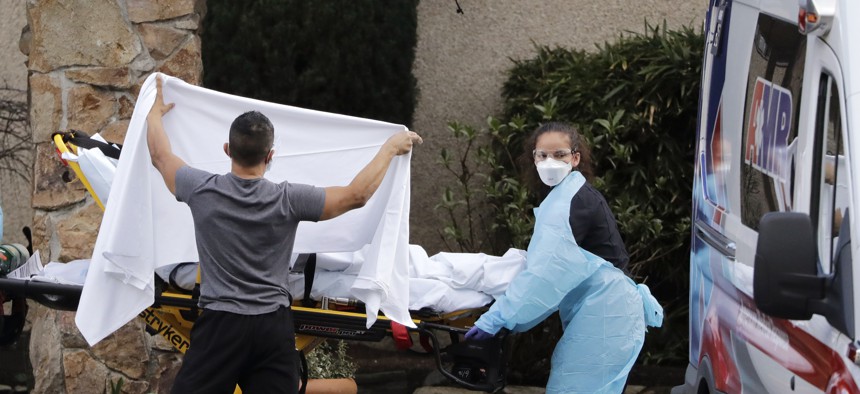 A staff member blocks the view as a person was taken on Feb. 29, 2020 by a stretcher to a waiting ambulance from a nursing facility where dozens of people were sick and being tested for the COVID-19 virus in Kirkland, Wash. 