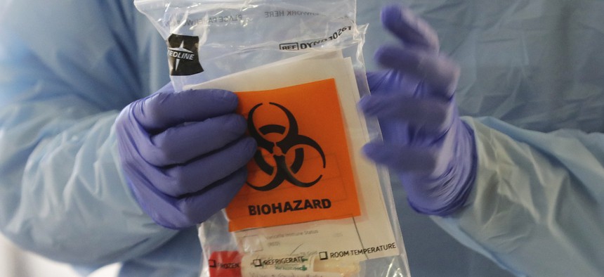 A nurse at a drive up COVID-19 coronavirus testing station, set up by the University of Washington Medical Center, holds a bag containing a swab used to take a sample from the nose of a person in their car, Friday, March 13, 2020, in Seattle.