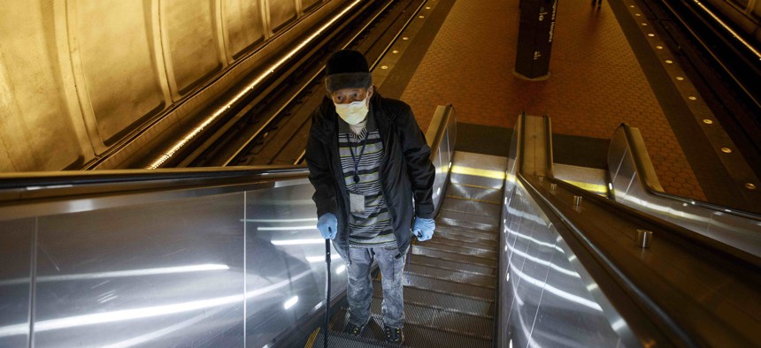 Andre of Washington, D.C., rides the escalator up at the Metro subway Congress Heights train station in Washington, Friday, March, 13, 2020. He wears two face masks and gloves to protect his children and grandchildren from the coronavirus.