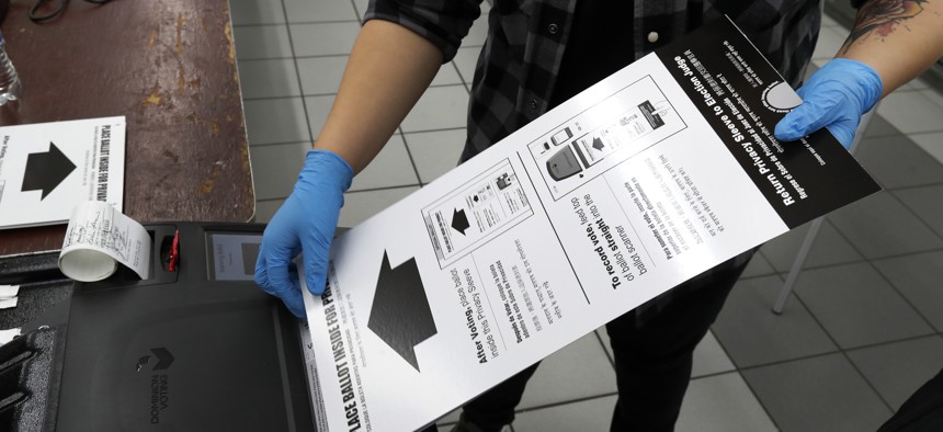 A poll worker at the Su Nueva Lavanderia polling place uses rubber gloves as she enters a ballot in the ballot box Tuesday, March 17, 2020, in Chicago.