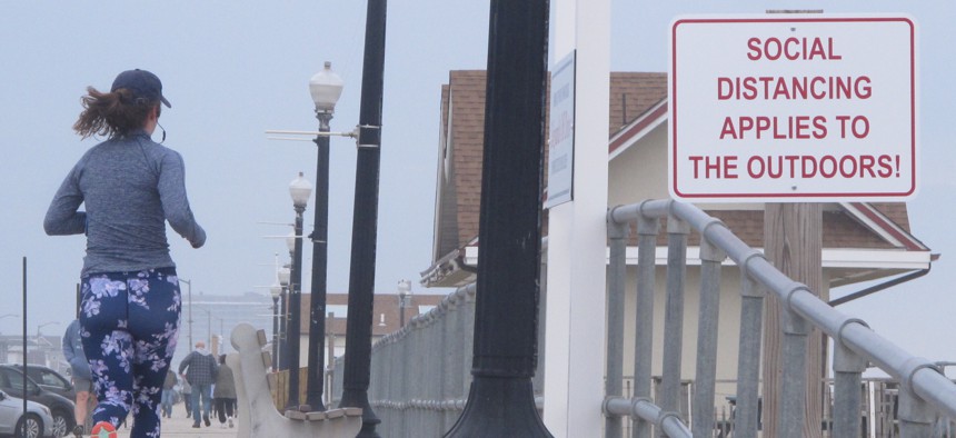 This March 20, 2020 photo shows a jogger running past a sign on the Bradley beach, N.J. oceanfront urging people to use "social distancing" to maintain space between each other even in the outdoors during the coronavirus outbreak.