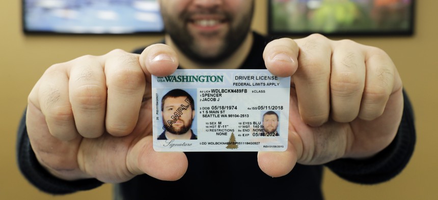 Ryan Norris, a license service representative at the Washington state Dept. of Licensing office in Lacey, Wash., poses for a photo Friday, June 22, 2018 while holding a sample copy of a Washington drivers license. 